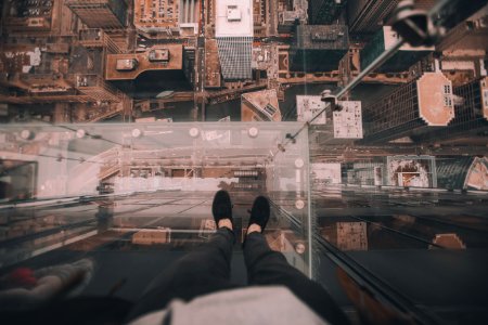 man standing on glass platform on top of building looking down on ground at daytime photo