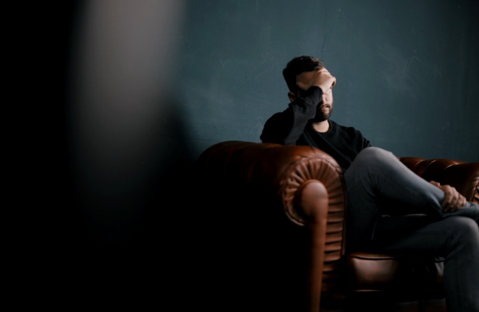 a man holds his head while sitting on a sofa