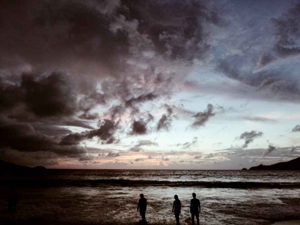 silhouette of three people on seashore under gray cloudy skies