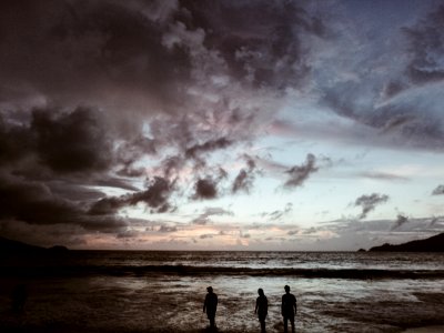 silhouette of three people on seashore under gray cloudy skies photo