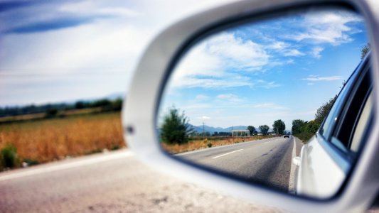 vehicle side mirror viewing car on the road during day