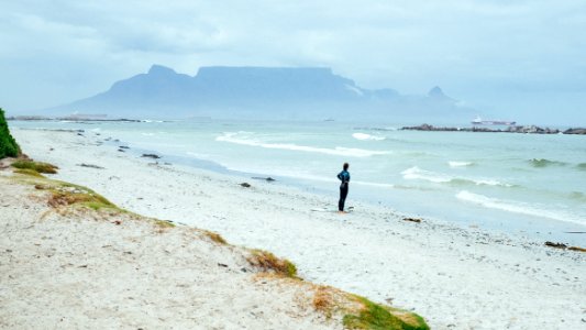 person standing on shore near mountain covering of fogs at daytime photo