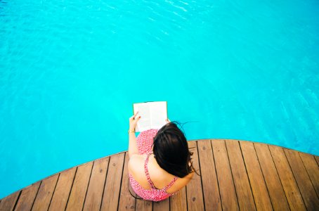 woman sitting on poolside dock while riding book photo