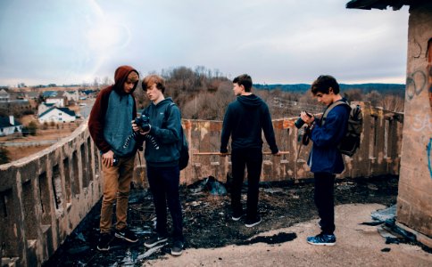 four man wearing blue jackets standing beside house looking at their cameras during daytime photo