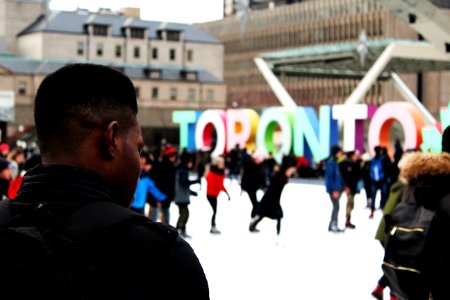 man wearing black backpack ice skating with other people near Toronto freestanding decor during daytime photo