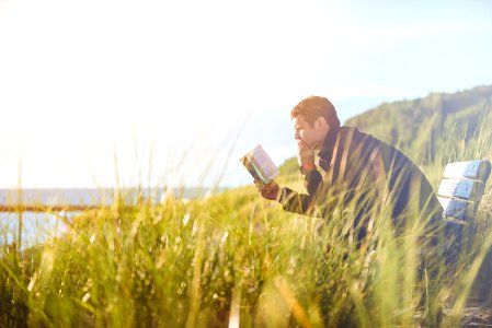 man reading book on beach near lake during daytime photo