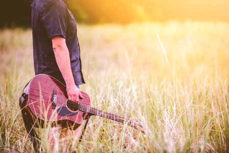 man carrying brown cutaway acoustic guitar standing on green grass field photo