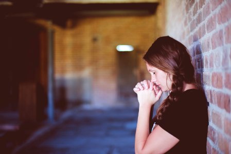 woman praying while leaning against brick wall photo