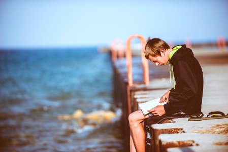 boy sitting on dock while reading photo