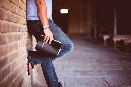 man holding Holy Bible leaning on bricked wall photo