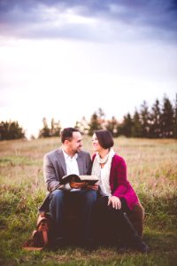 photo of man reading book to woman under grey cloudy sky photo