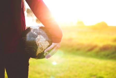 person holding black and brown globe ball while standing on grass land golden hour photography