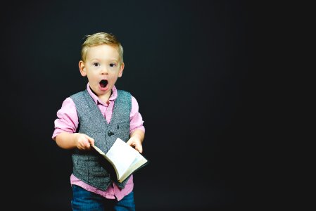 boy wearing gray vest and pink dress shirt holding book