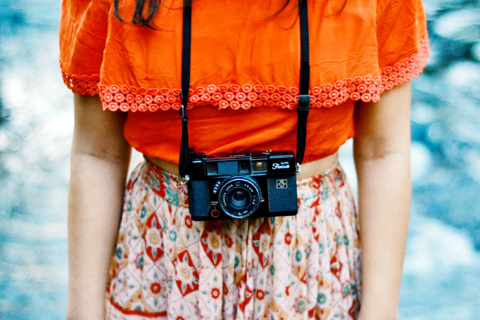 woman wearing orange and multicolored dress with black bridge camera on her neck