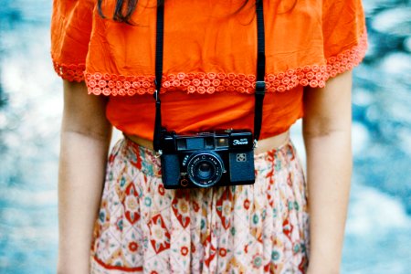 woman wearing orange and multicolored dress with black bridge camera on her neck