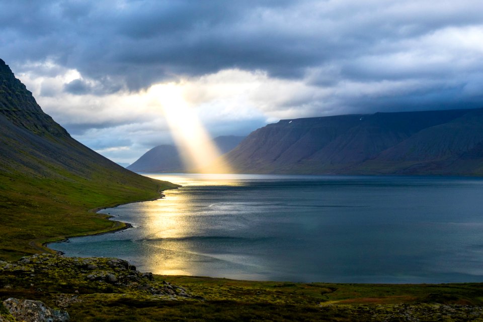 sun reflection on calm water near green mountains