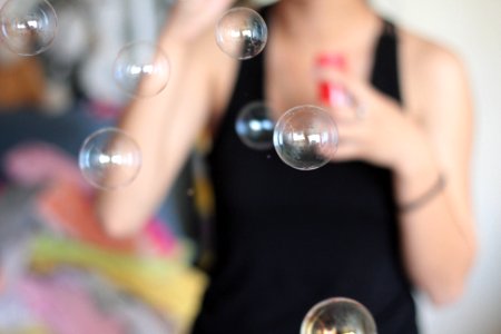 selective focus photo of bubbles blown by person wearing black tank top photo