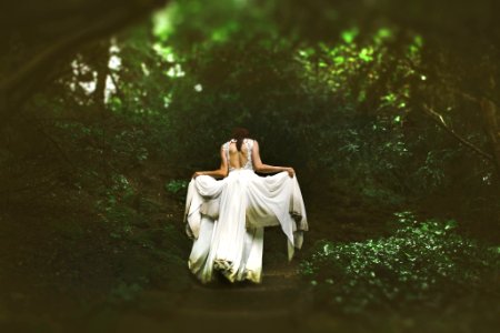 woman in white dress walking on pathway surrounded by trees photo