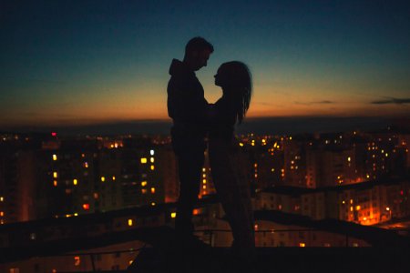 silhouette of man and woman standing on roof building photo