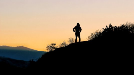 silhouette of person on top of hill during golden hour photo