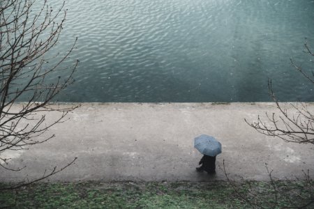 person with umbrella walking on road near body of water during daytime photo