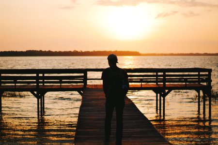 silhouette of man walking on dock during golden hour photo