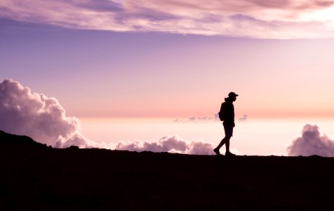 silhouette of person walking under white clouds photo