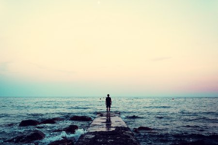 silhouette of person standing on sea dock under cloudy sky photo