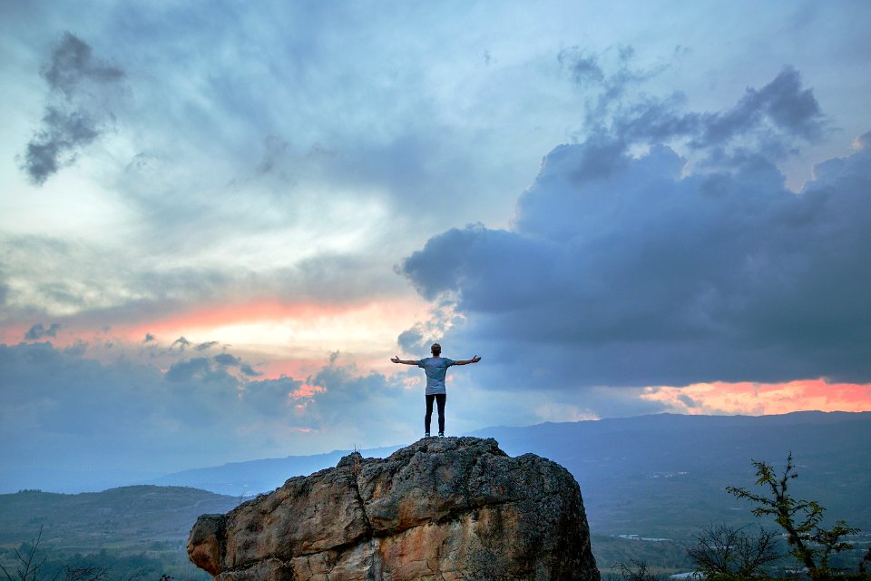 man standing on top of rock mountain during golden hour photo