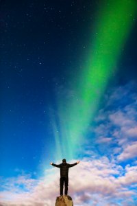 man standing on rock under green aurora borealis and white clouds photo