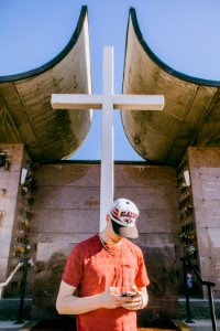 man holding smartphone and standing near cross statue photo