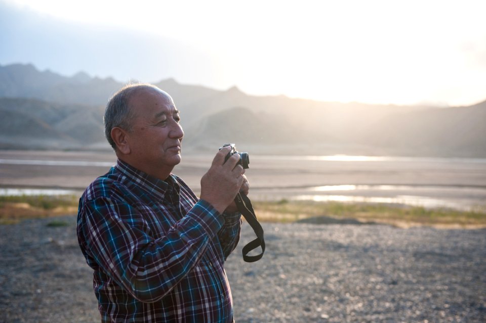 man holding camera standing with mountain background