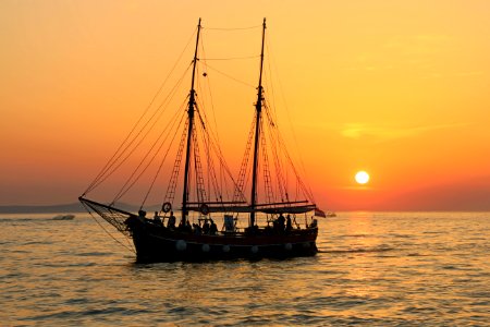 black and white sailboat in body of water during sunset