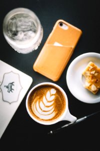 selective focus photo of cup of cappuccino beside smartphone, saucer, and glass photo