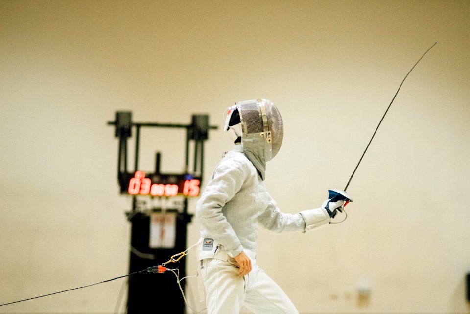 man wearing white coveralls holding fencing sword
