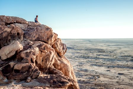 man sitting on top of rock formation near beach photo