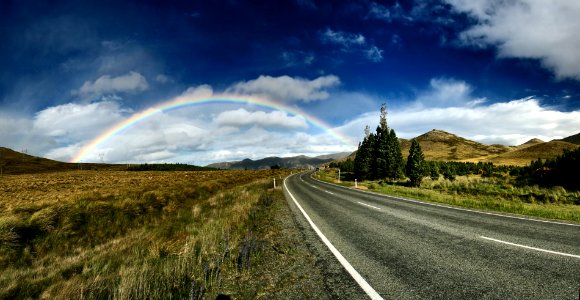 highway near trees and rainbow under blue sky