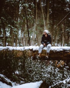 man wearing white knit cap and black jacket sitting on snow covered tree log photo
