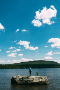 man in white shirt and blue denim jeans standing on seashore under blue and white cloudy photo