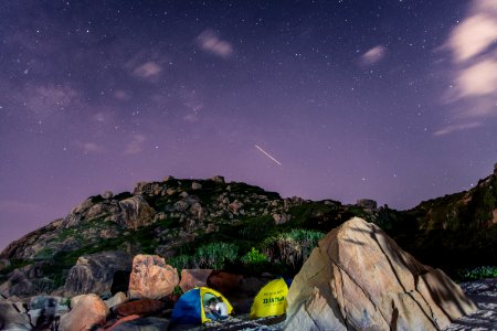 tents surrounded with green rocks under purple sky at night photo