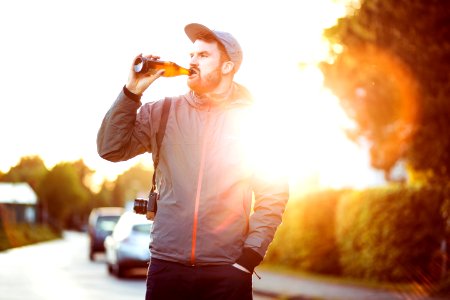 man in gray and pink zip-up hoodie holding bottle while drinking during daytime photo