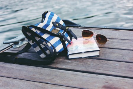 blue and white striped crossbody bag near book and sunglasses on sea dock during daytime photo