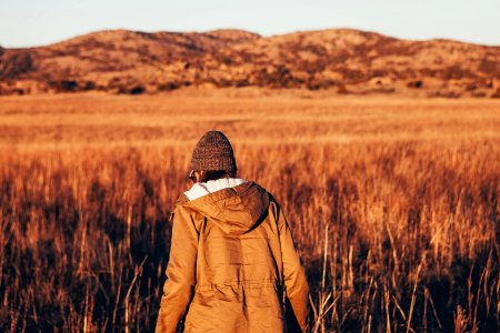 person wearing jacket walking in brown grass field photo