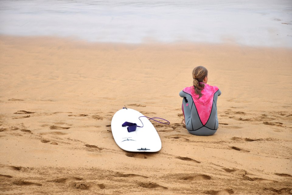 woman sitting on shore beside surfboard near sea