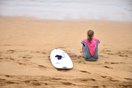woman sitting on shore beside surfboard near sea photo