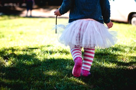 toddler girl wearing teal and white polka-dot long-sleeved shirt and white tutu skirt outfit walking on green sod at daytime photo