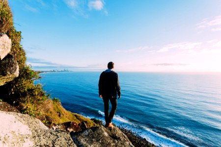 man standing on rock cliff near sea