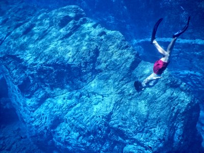 man in red shorts swimming near huge underwater rock photo