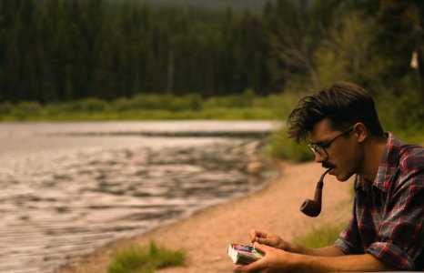 man smoking on pipe beside lake photo