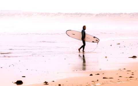 man holding surf board while standing on shore at daytime photo